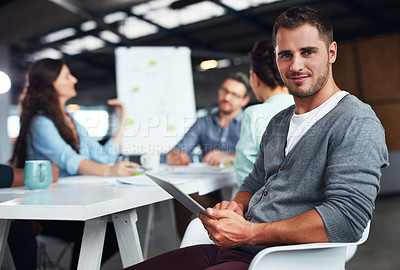 Buy stock photo Portrait of a man sitting at a table in an office using a digital tablet with colleagues working in the background