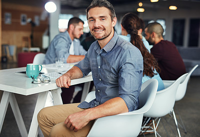 Buy stock photo Portrait of a mature man sitting at a table in an office with colleagues working in the background