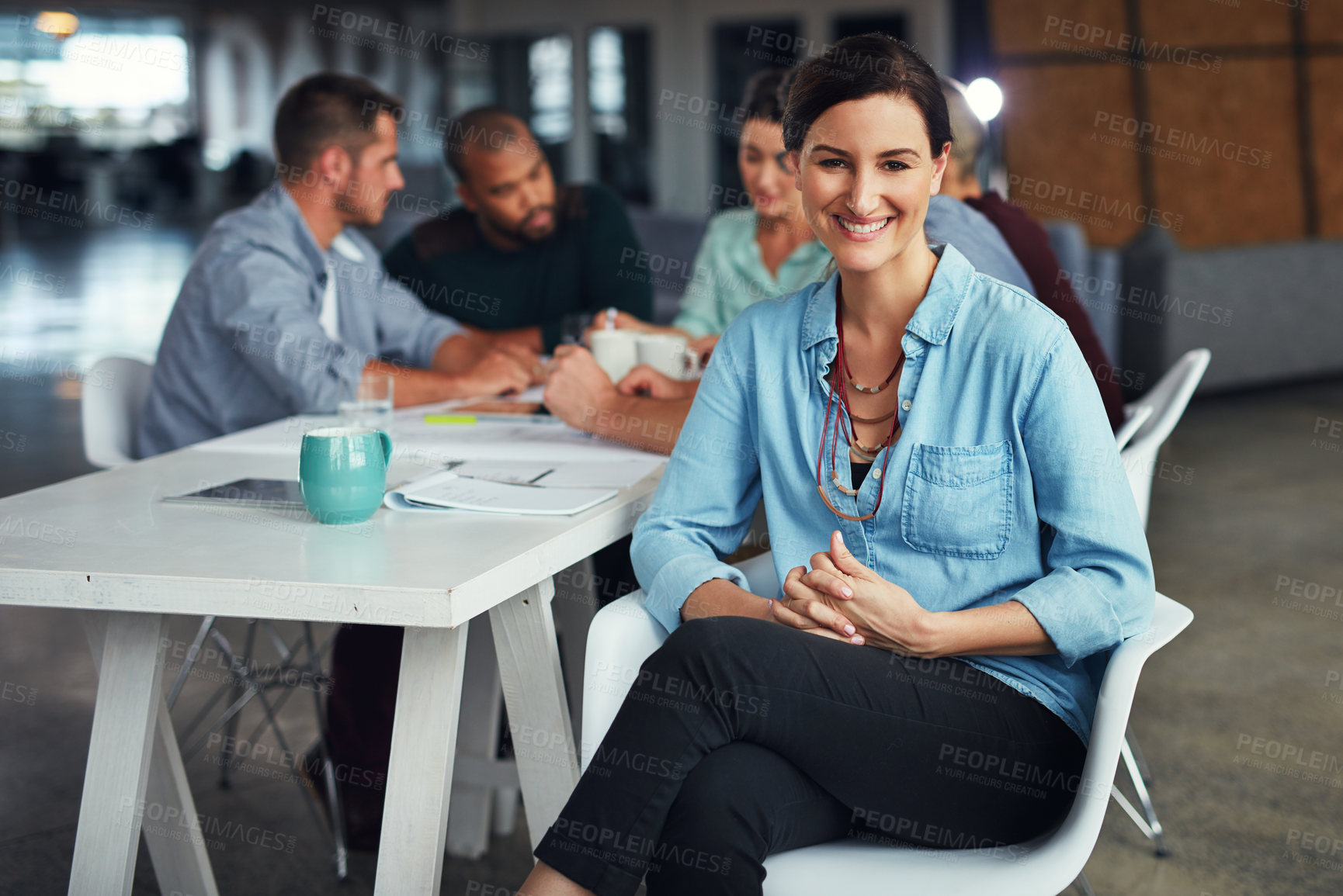 Buy stock photo Portrait of a young woman sitting at a table in an office with colleagues working in the background