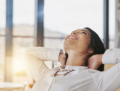 Buy stock photo Shot of a content young businesswoman sitting in her office with her hands behind her head