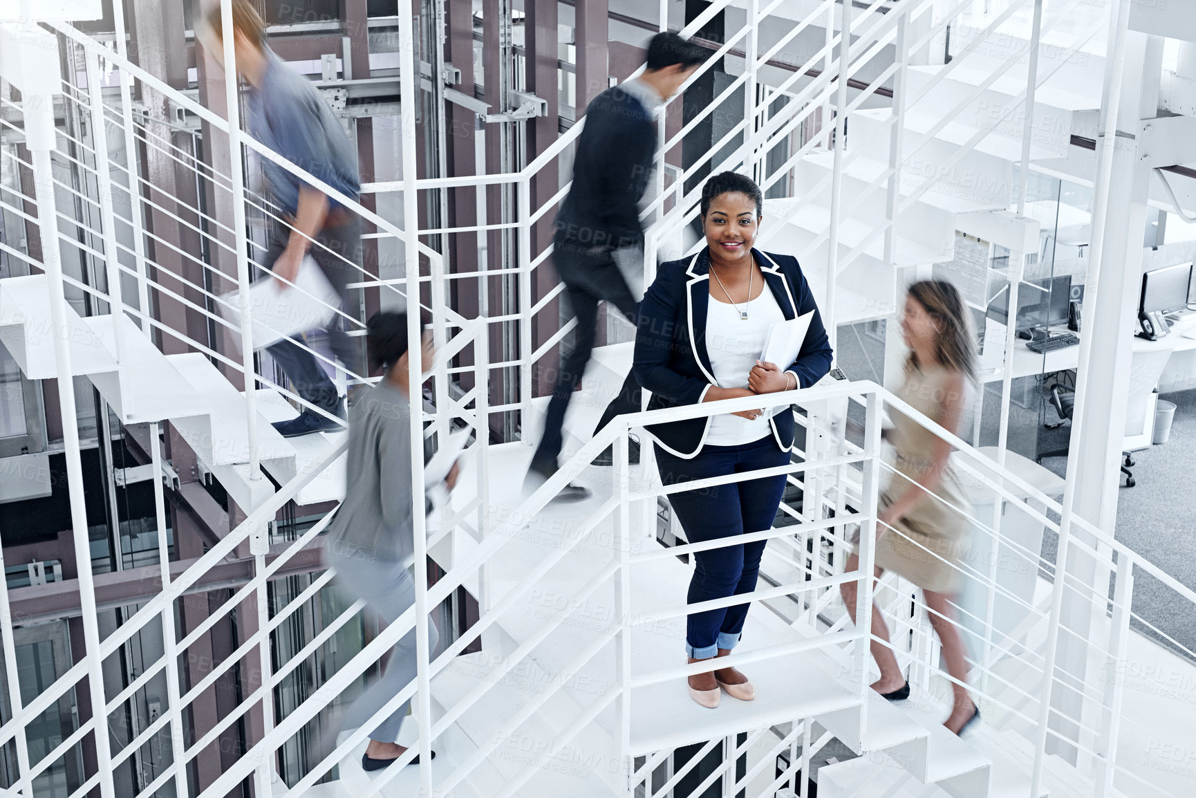 Buy stock photo Portrait of a young professional standing on a stairs with colleagues rushing around her