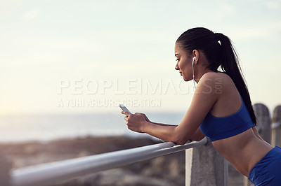 Buy stock photo Shot of a fit young woman using her phone and earphones during a workout outdoors