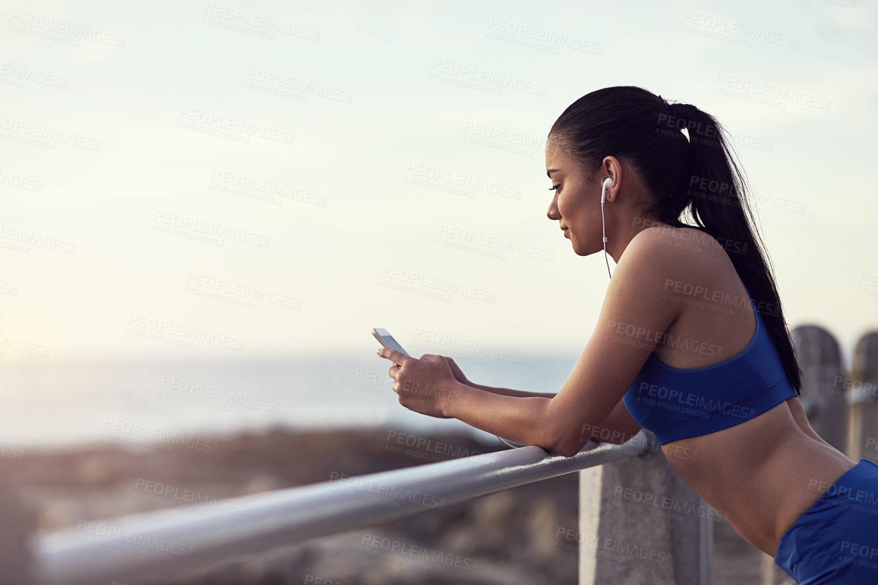 Buy stock photo Girl, phone and music with fitness outdoor at promenade with break from exercise, workout and runner. Athlete, woman and earphones with typing, text message and communication with mockup by railing