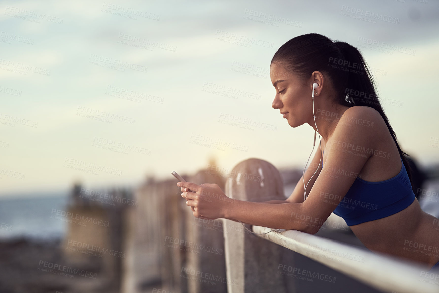 Buy stock photo Girl, phone and earphones with fitness outdoor at promenade with break from exercise, workout and runner. Athlete, woman and music with typing, text message and communication with mockup by railing