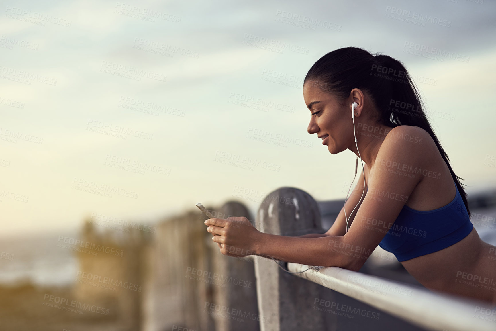 Buy stock photo Woman, phone and earphones with fitness outdoor at promenade with break from exercise, workout and runner. Athlete, girl and music with typing, text message and communication with mockup by railing