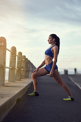Buy stock photo Shot of a fit young woman warming up during her workout outdoors