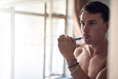 Buy stock photo Shot of a young man brushing his teeth while looking at himself in the mirror