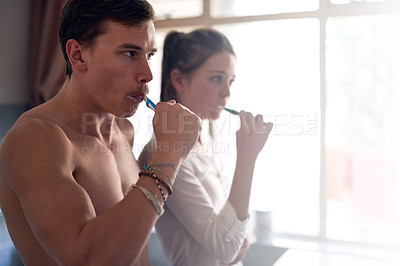 Buy stock photo Shot of a young couple brushing their teeth together while standing in the bathroom