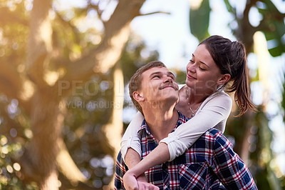 Buy stock photo Shot of a happy young couple enjoying a piggyback ride outside