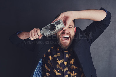 Buy stock photo Shot of a trendy young man with a vintage camera posing against a dark background