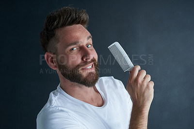 Buy stock photo Portrait of a handsome young man posing against a dark background with a comb in his hand