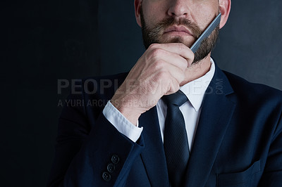 Buy stock photo Shot of an unidentifiable businessman grooming his beard with a comb against a dark background