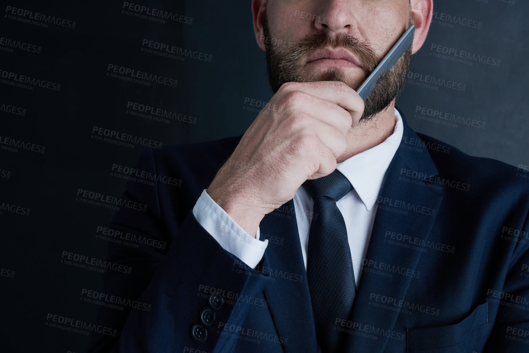 Buy stock photo Shot of an unidentifiable businessman grooming his beard with a comb against a dark background