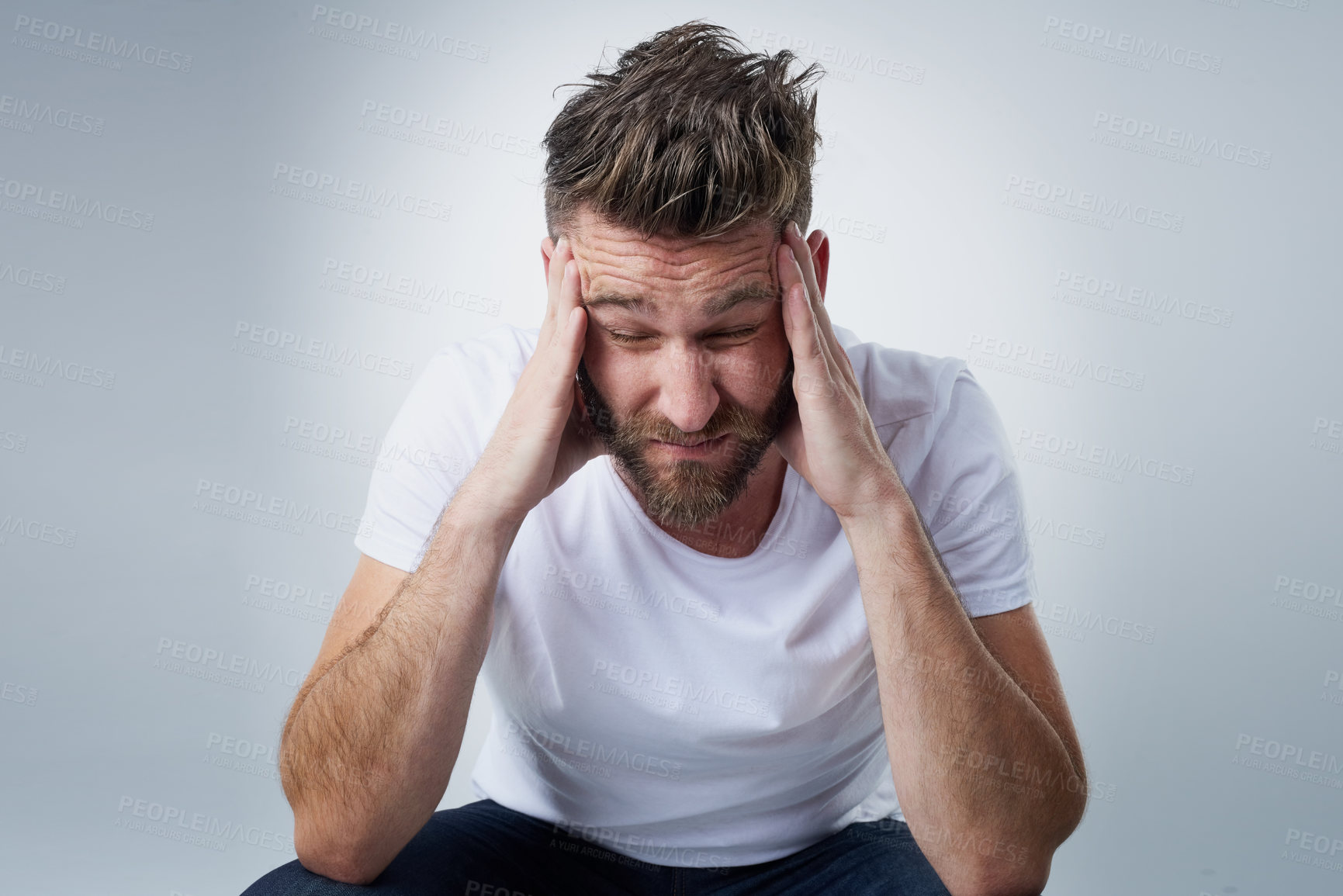 Buy stock photo Shot of a young man with a headache holding his head while sitting on a chair in the studio
