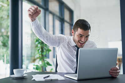 Buy stock photo Shot of a young businessman cheering while working on a laptop in an office