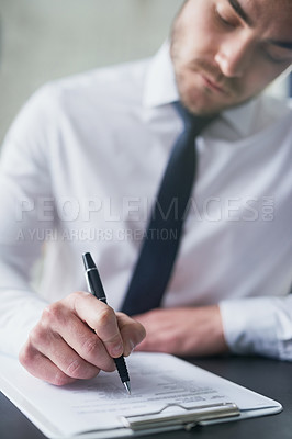 Buy stock photo Cropped shot of a young businessman filling out paperwork on a clipboard while sitting at a table in an office