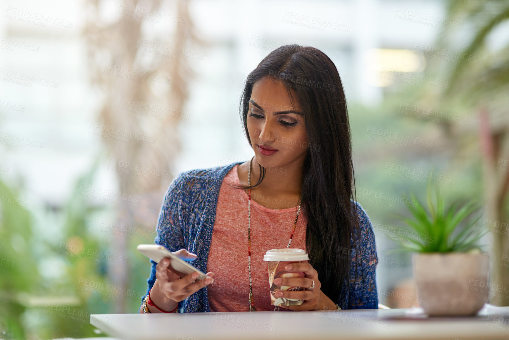 Buy stock photo Shot of an attractive young woman using her cellphone while drinking coffee in a coffee shop
