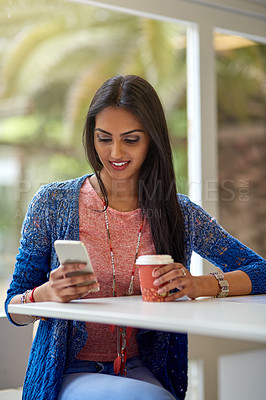 Buy stock photo Shot of an attractive young woman using her cellphone while drinking coffee in a coffee shop