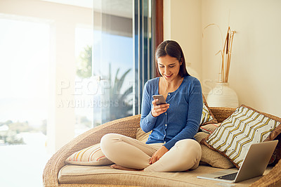 Buy stock photo Shot of a happy young woman using her smartphone while relaxing in her lounge at home