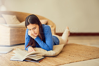 Buy stock photo Shot of a young woman reading a book on her lounge floor at home