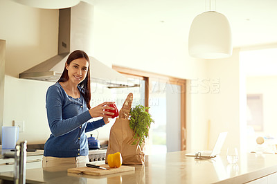 Buy stock photo Portrait of a happy young woman unpacking a bag of groceries in her kitchen at home