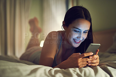 Buy stock photo Shot of a young woman using a cellphone while lying on her bed in her bedroom