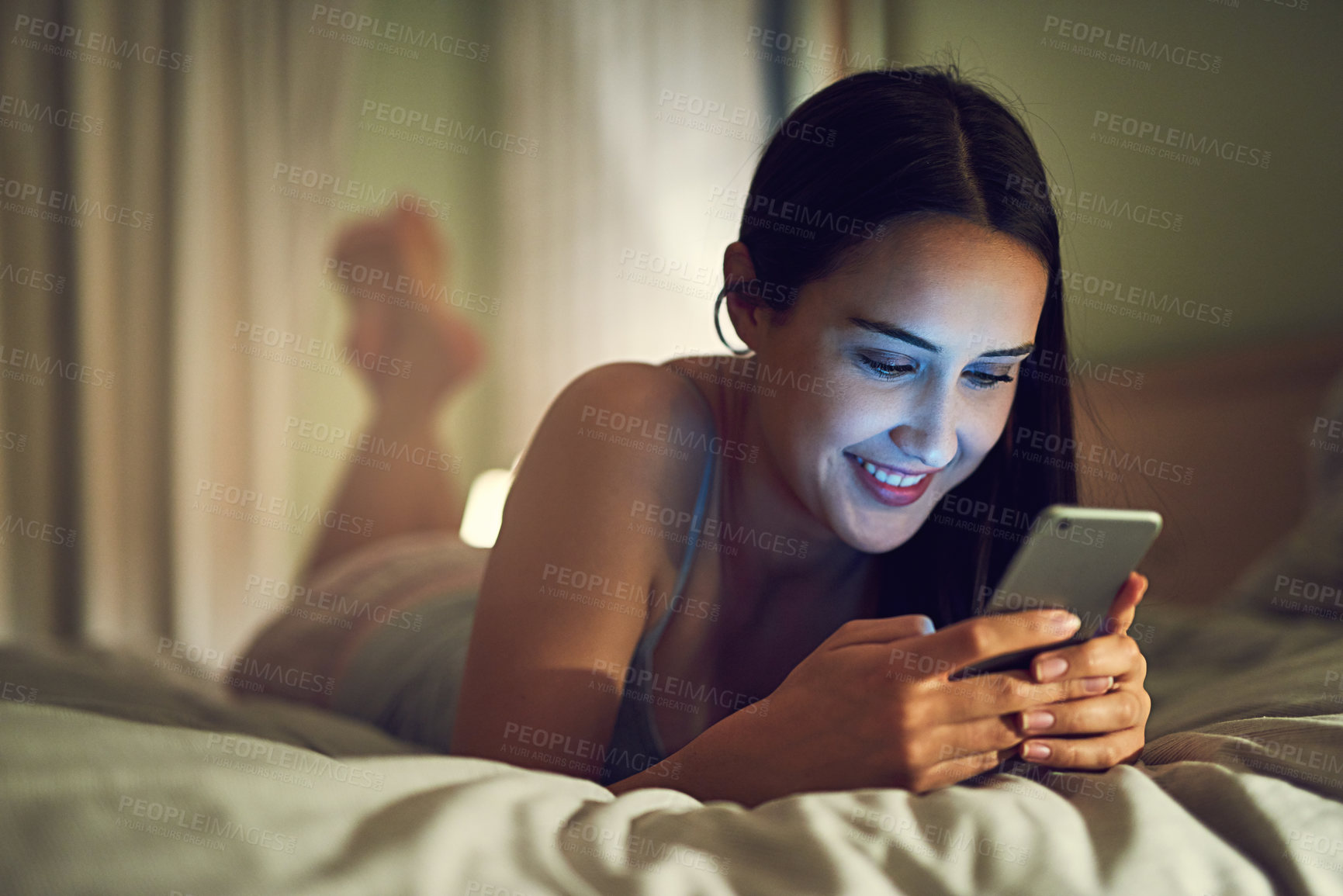 Buy stock photo Shot of a young woman using a cellphone while lying on her bed in her bedroom