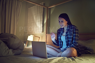 Buy stock photo Shot of a young woman video chatting on a laptop at night while sitting on her bed in her bedroom