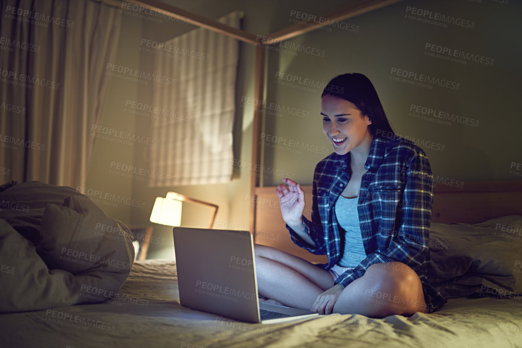 Buy stock photo Shot of a young woman video chatting on a laptop at night while sitting on her bed in her bedroom