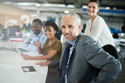 Buy stock photo Portrait of a mature man sitting at a table in an office with colleagues in the background