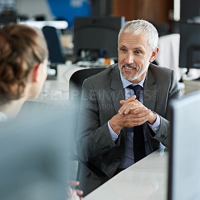 Buy stock photo Shot of two colleagues talking together while sitting at a desk in an office