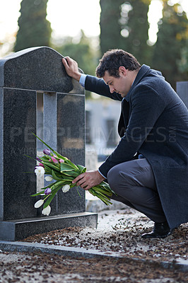 Buy stock photo Shot of a young man visiting a gravesite with a bunch of flowers