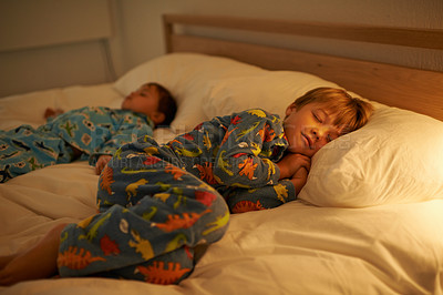 Buy stock photo Brothers, bed and rest for night, sleeping and tired with fatigue and peace. Children, dreaming and exhausted with pyjamas, onesie and bedroom with lamp for serene childhood at home or house for kids