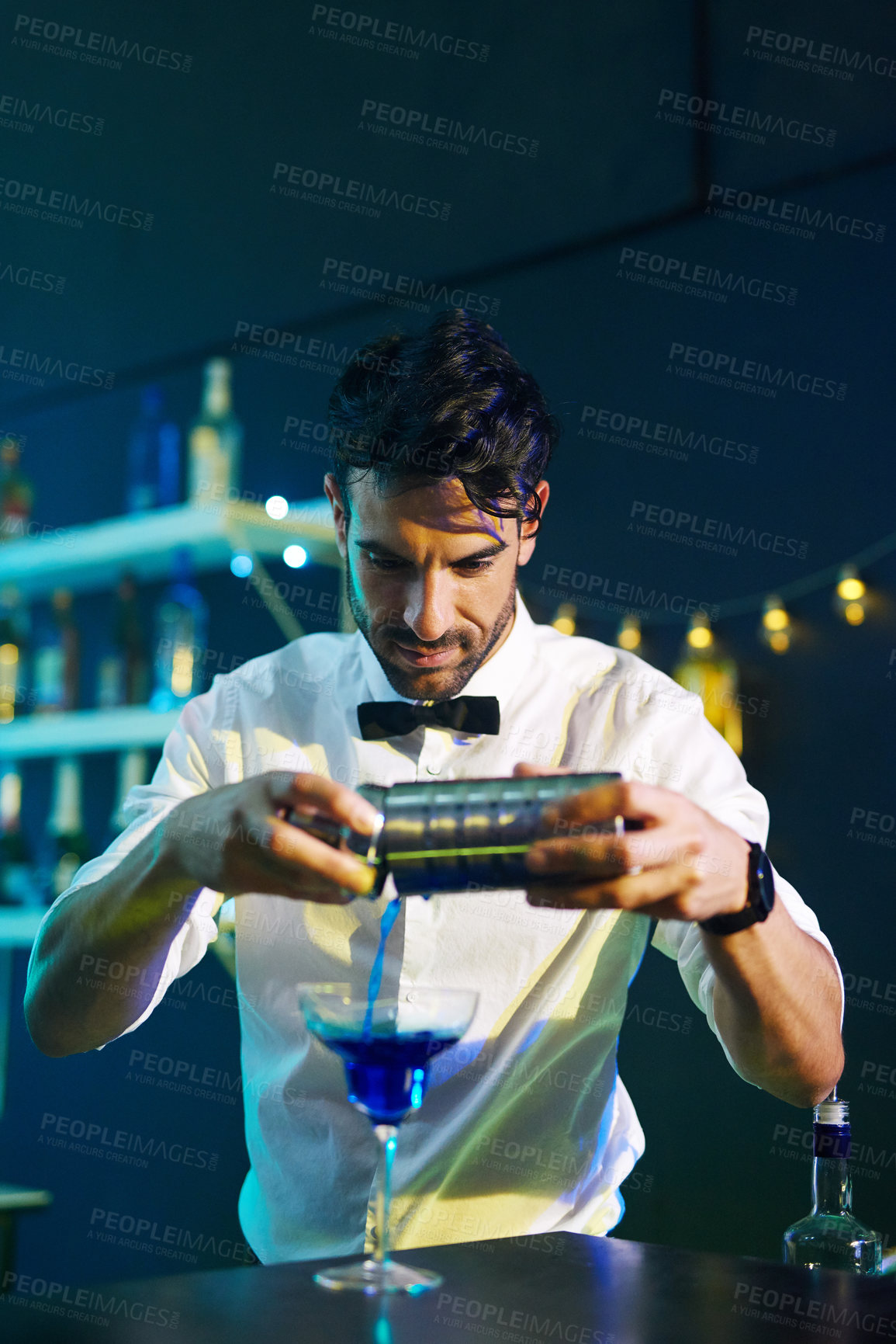 Buy stock photo Shot of a handsome young barman pouring a cocktail into a glass in a night club