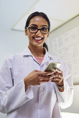 Buy stock photo Portrait of a young female dentist texting on her cellphone in her office