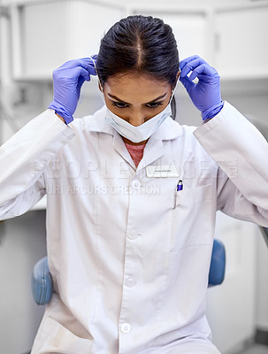 Buy stock photo Cropped shot of a young female dentist putting on a surgical mask