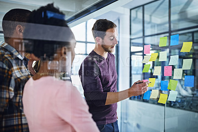 Buy stock photo Cropped shot of a team of designers brainstorming with notes on a glass wall in an office