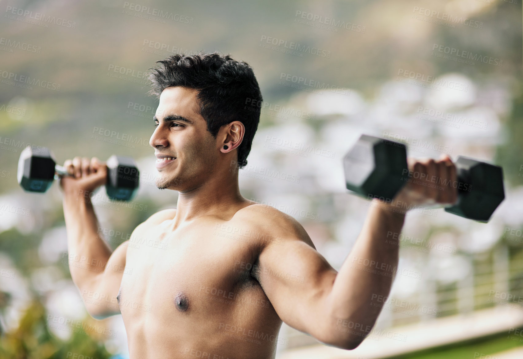 Buy stock photo Shot of a shirtless young man working out with dumbbells outside