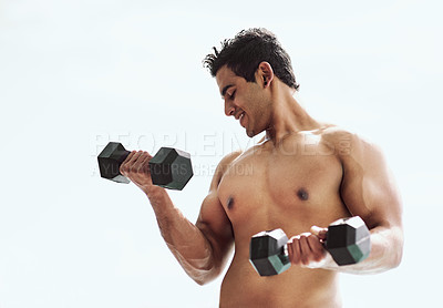 Buy stock photo Shot of a shirtless young man working out with dumbbells outside