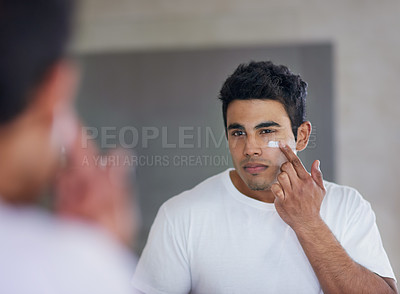 Buy stock photo Shot of a handsome young man applying moisturizer to his face