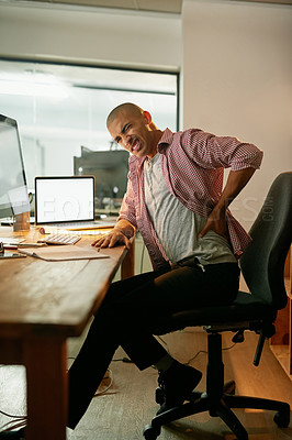 Buy stock photo Shot of a young designer experiencing back pain while working late at his desk