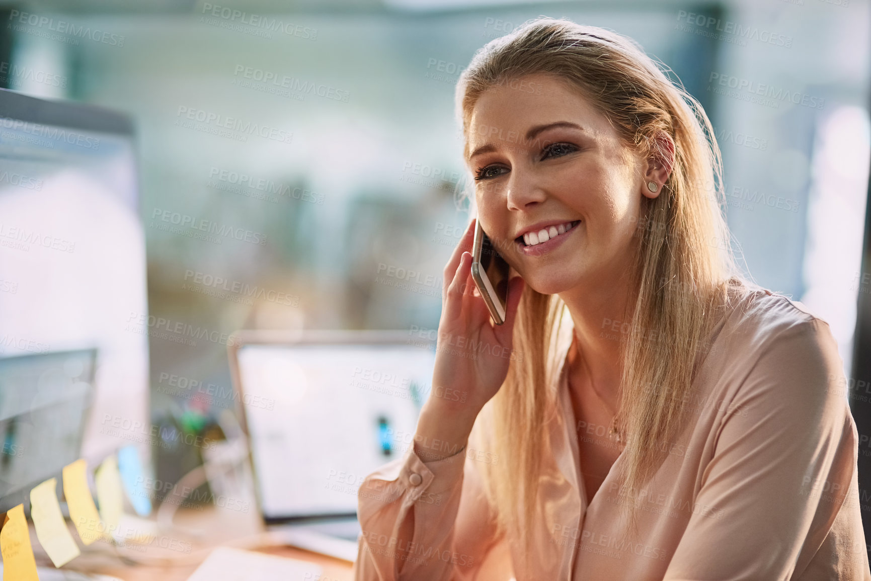 Buy stock photo Shot of a smiling young businesswoman talking on a cellphone while sitting at her desk in an office