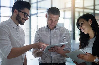 Buy stock photo Shot of three colleagues using digital tablets while standing together in an office