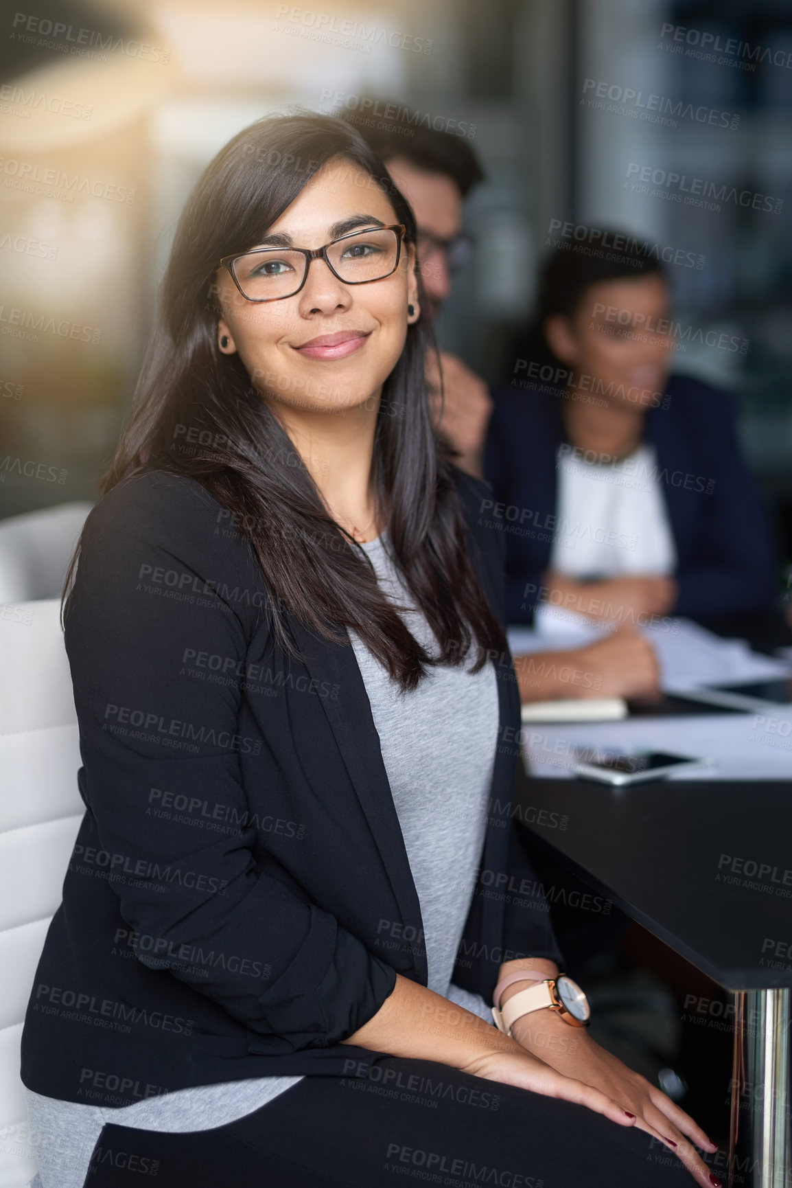 Buy stock photo Portrait of a smiling young businesswoman sitting in an office with colleagues in the background