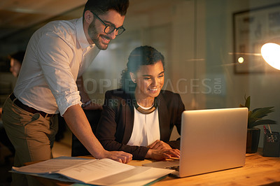 Buy stock photo Shot of a young businessman helping his colleague with her laptop while they work overtime in the office