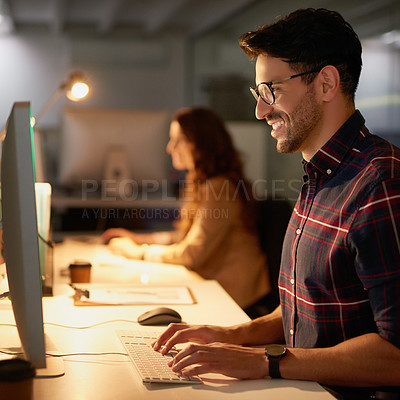 Buy stock photo Shot of two businesspeople using their computers while working overtime in the office