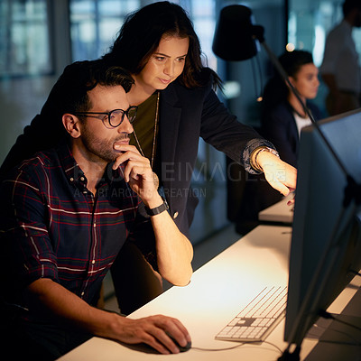 Buy stock photo Shot of a businesswoman helping her colleague with his computer while they work overtime in the office