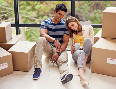 Buy stock photo Shot of a young couple sitting on the floor while taking a break from moving into a new home
