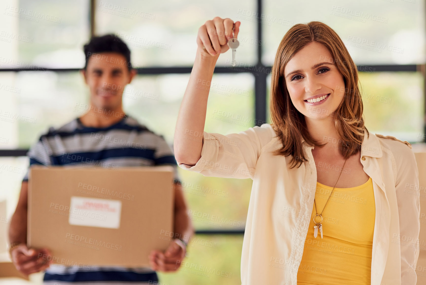 Buy stock photo Portrait of a young woman holding up the keys to a new home with her boyfriend carrying boxes in the background