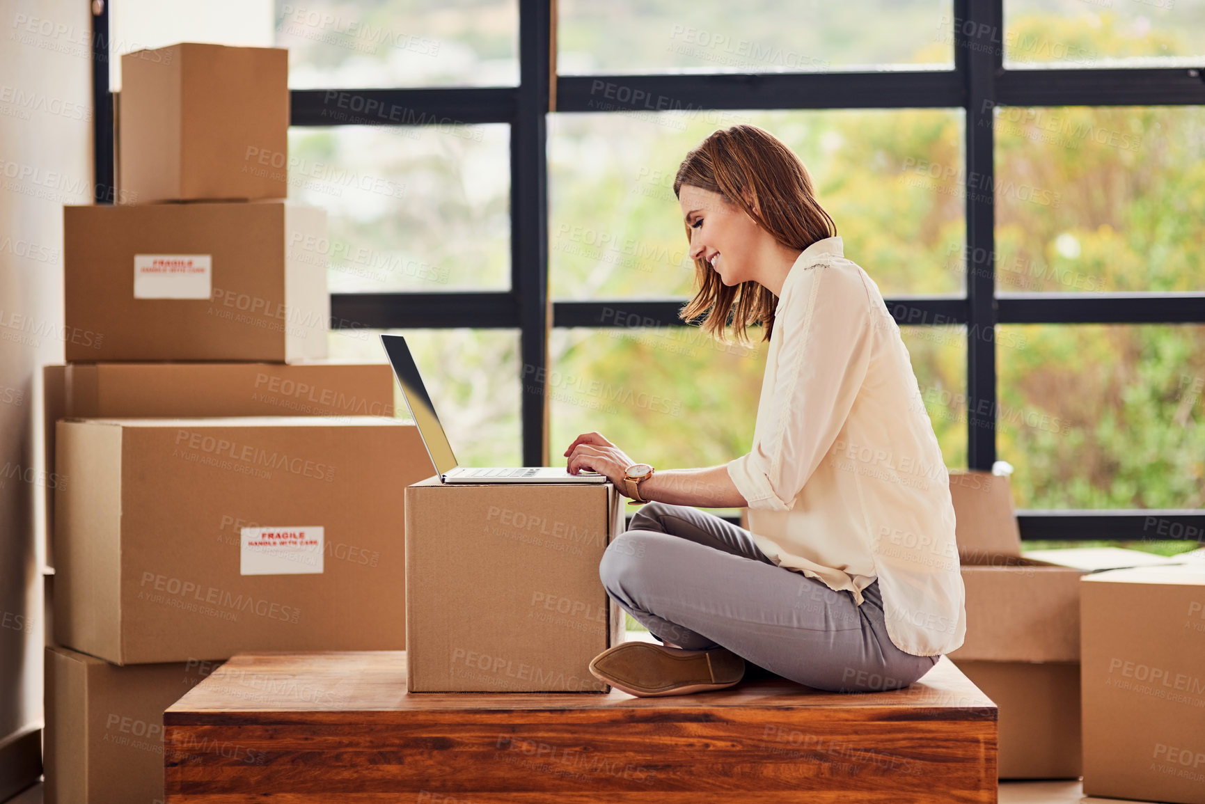 Buy stock photo Shot of a young woman using a laptop while taking a break from moving into a new home